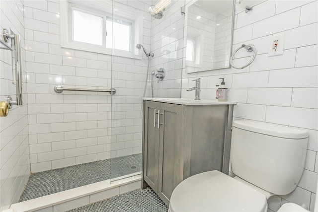 bathroom with vanity, a shower with door, tile walls, and toilet