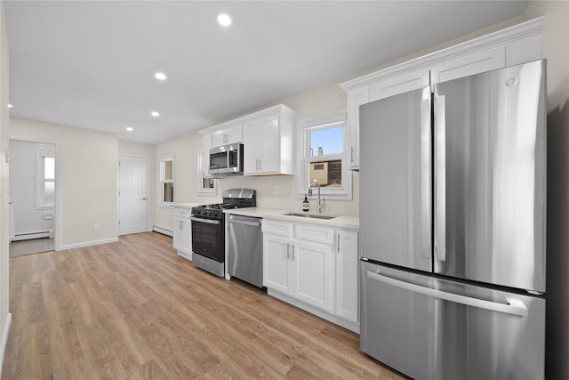 kitchen with sink, light hardwood / wood-style flooring, appliances with stainless steel finishes, white cabinetry, and a baseboard heating unit