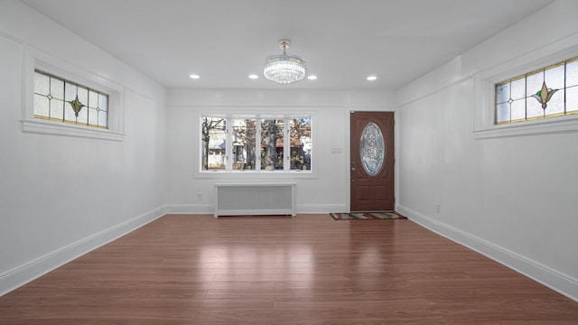 foyer with dark wood-type flooring, radiator, an inviting chandelier, and a wealth of natural light