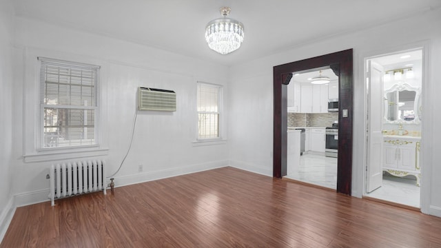 unfurnished room with an inviting chandelier, hardwood / wood-style flooring, radiator heating unit, and an AC wall unit