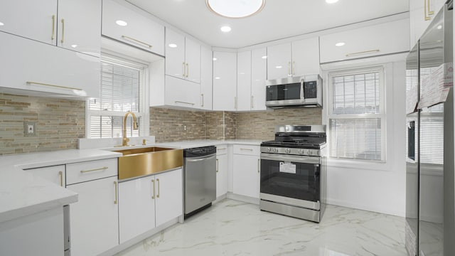 kitchen featuring sink, white cabinets, decorative backsplash, stainless steel appliances, and light stone countertops