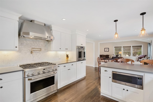 kitchen with tasteful backsplash, wall chimney range hood, open floor plan, appliances with stainless steel finishes, and dark wood-style flooring