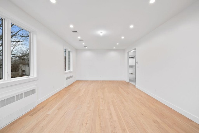 unfurnished room featuring a healthy amount of sunlight, radiator heating unit, and light wood-type flooring