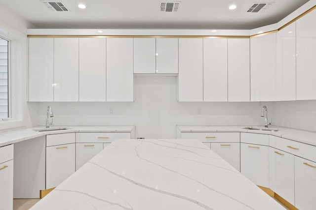 kitchen with light stone countertops, sink, and white cabinets