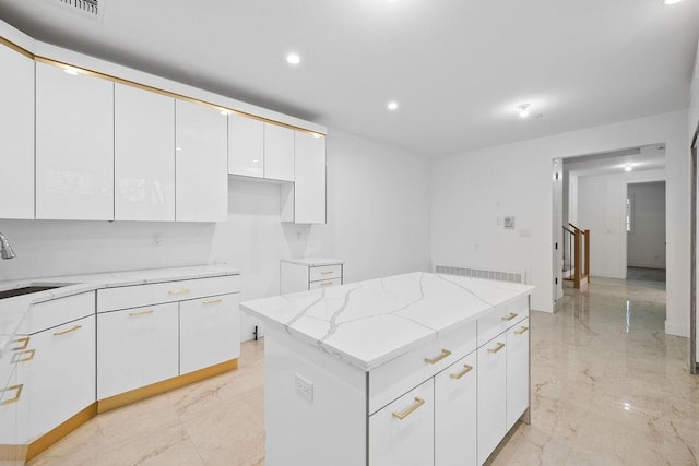 kitchen with sink, light stone countertops, white cabinets, and a kitchen island