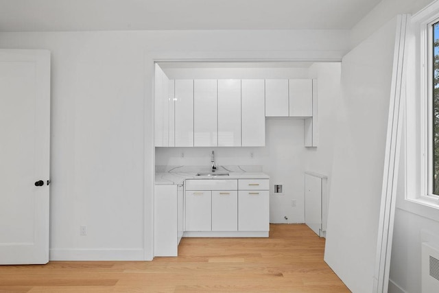 kitchen featuring light stone counters, light hardwood / wood-style floors, sink, and white cabinets