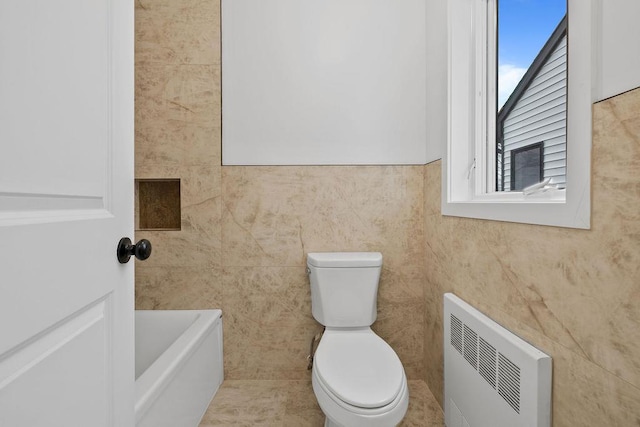 bathroom with a tub to relax in, toilet, radiator, and tile walls