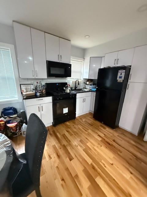 kitchen with sink, light hardwood / wood-style flooring, black appliances, and white cabinets