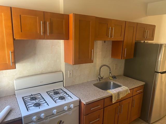 kitchen with sink, light stone counters, stainless steel fridge, white gas range, and backsplash