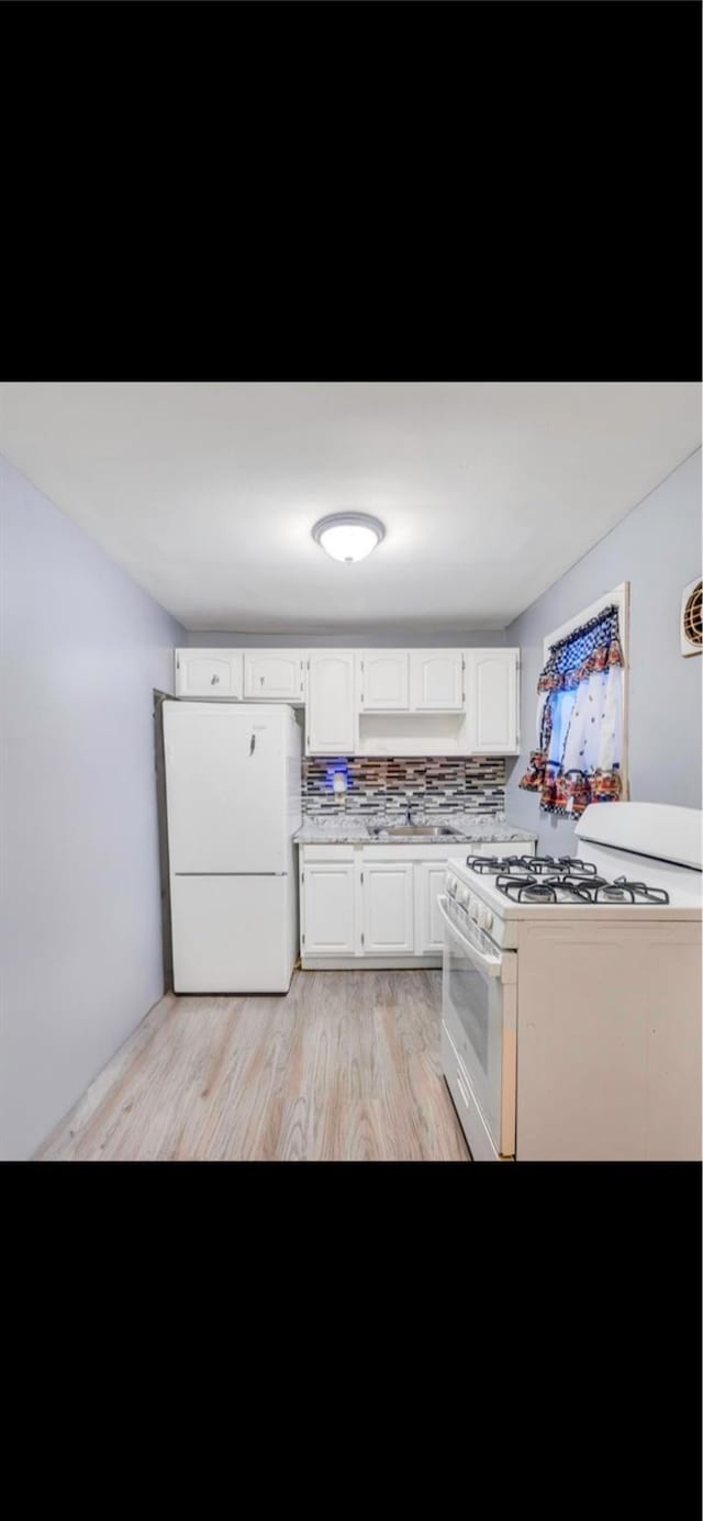 kitchen with sink, white appliances, white cabinetry, tasteful backsplash, and light hardwood / wood-style floors