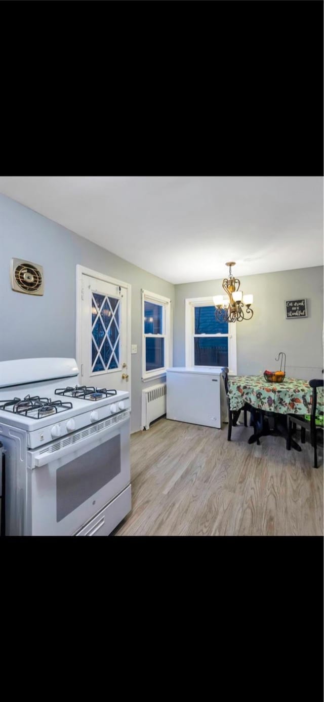 kitchen with a chandelier, white gas range, radiator, and light wood-type flooring