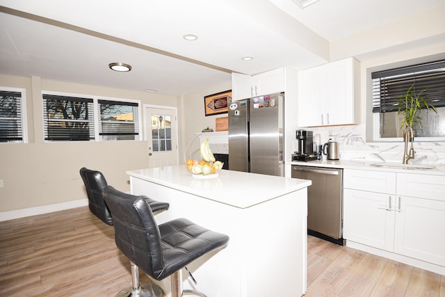 kitchen featuring appliances with stainless steel finishes, white cabinetry, sink, backsplash, and light hardwood / wood-style floors