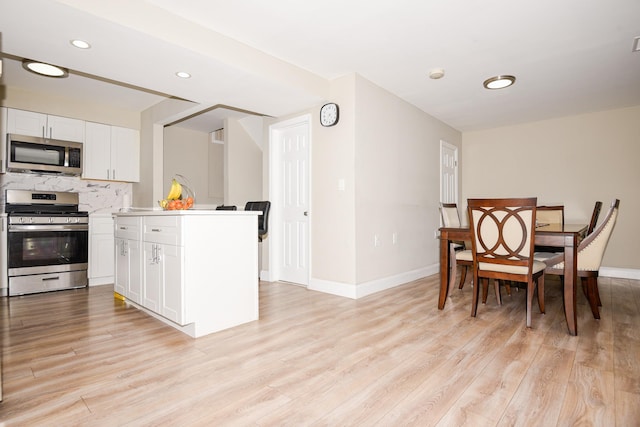 kitchen featuring backsplash, appliances with stainless steel finishes, light hardwood / wood-style floors, and white cabinets