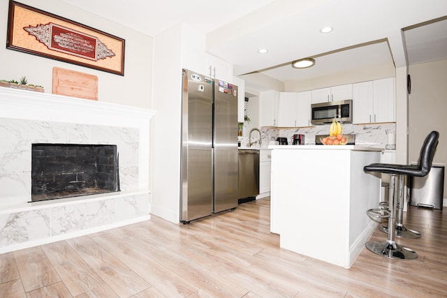 kitchen featuring sink, stainless steel appliances, white cabinets, decorative backsplash, and light wood-type flooring