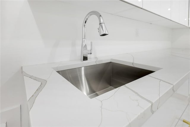 room details with white cabinetry, light stone countertops, and sink