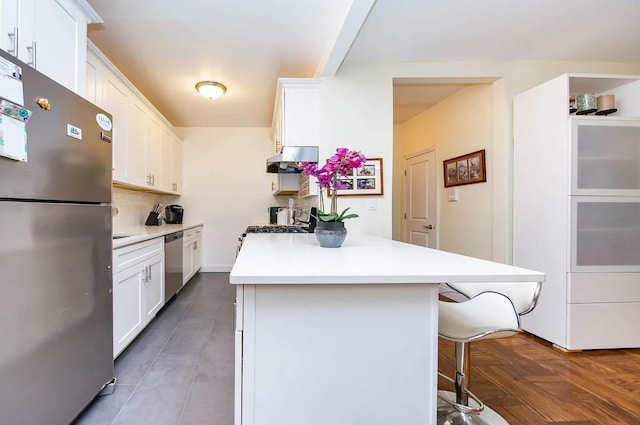 kitchen with white cabinetry, parquet flooring, appliances with stainless steel finishes, and a breakfast bar area