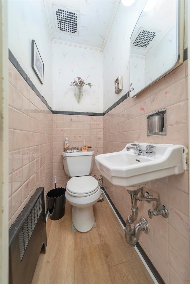 bathroom with toilet, heating unit, crown molding, tile walls, and hardwood / wood-style floors