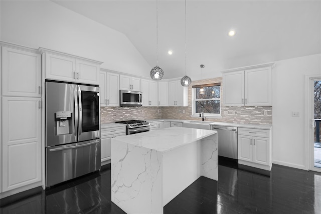 kitchen featuring white cabinetry, light stone counters, hanging light fixtures, a kitchen island, and stainless steel appliances