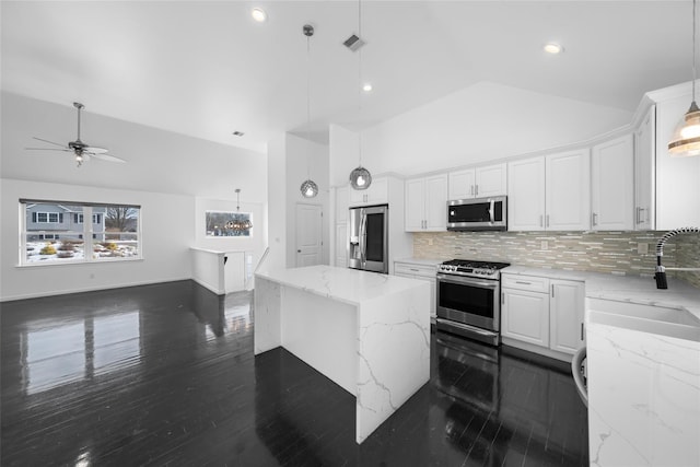 kitchen with a kitchen island, appliances with stainless steel finishes, decorative light fixtures, white cabinets, and light stone counters