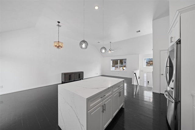 kitchen with decorative light fixtures, stainless steel fridge, white cabinets, a center island, and light stone counters