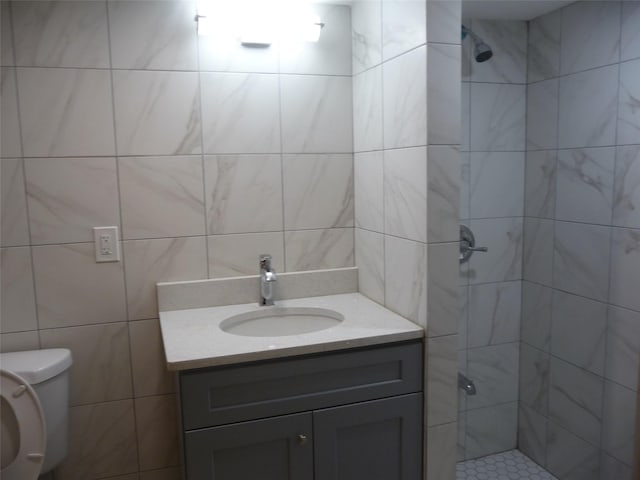 bathroom with vanity, a tile shower, tile walls, and toilet