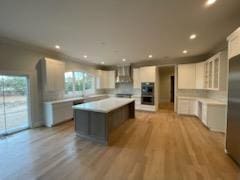 kitchen featuring a center island, light hardwood / wood-style flooring, white cabinets, wall chimney range hood, and backsplash