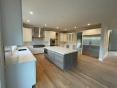 kitchen featuring sink, hardwood / wood-style floors, white cabinets, a kitchen island, and wall chimney exhaust hood