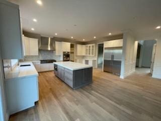 kitchen featuring white cabinetry, high quality fridge, a kitchen island, wall chimney exhaust hood, and light wood-type flooring