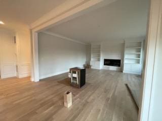 unfurnished living room featuring hardwood / wood-style flooring, ornamental molding, and built in shelves