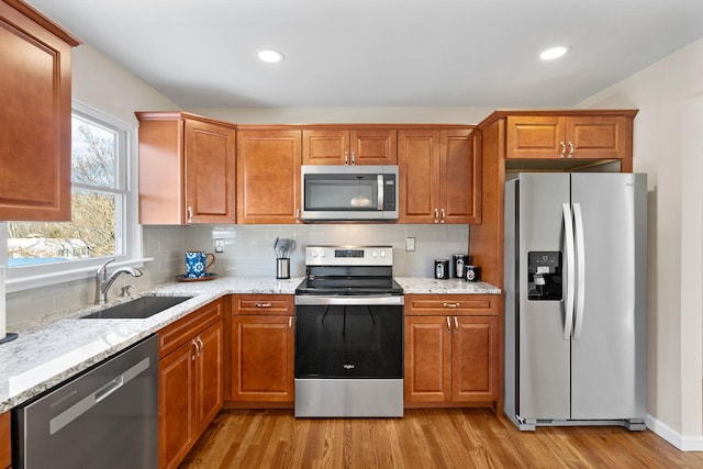 kitchen with sink, light stone counters, light wood-type flooring, appliances with stainless steel finishes, and backsplash