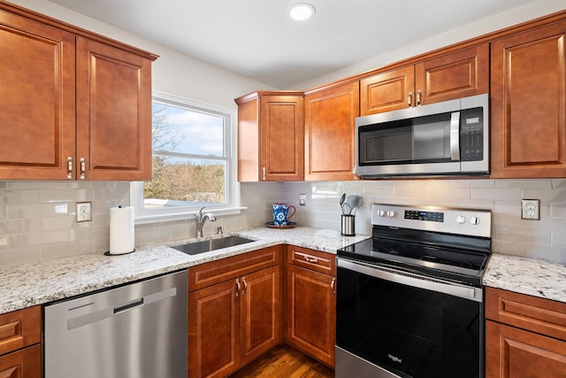 kitchen with stainless steel appliances, light stone countertops, sink, and backsplash