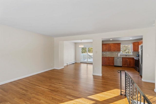 unfurnished living room featuring baseboard heating, a notable chandelier, sink, and light wood-type flooring