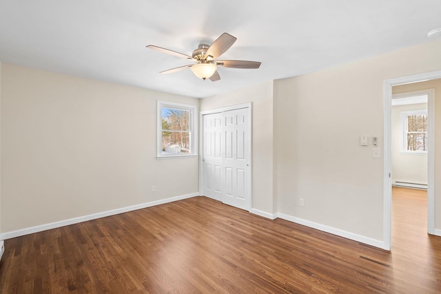 unfurnished bedroom with multiple windows, a baseboard radiator, hardwood / wood-style flooring, and a closet