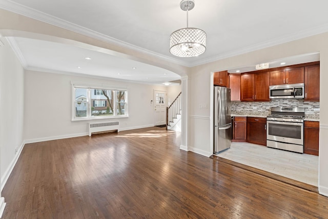 kitchen with radiator, appliances with stainless steel finishes, hanging light fixtures, tasteful backsplash, and light hardwood / wood-style floors