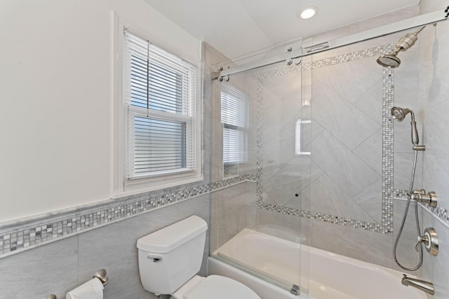 bathroom featuring bath / shower combo with glass door, tile walls, and toilet