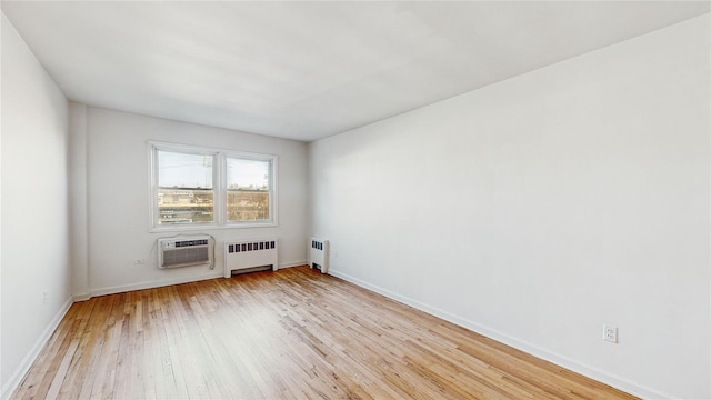 spare room featuring an AC wall unit, radiator heating unit, and light hardwood / wood-style floors