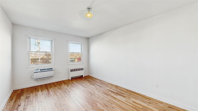 unfurnished room with radiator heating unit, light hardwood / wood-style flooring, and an AC wall unit