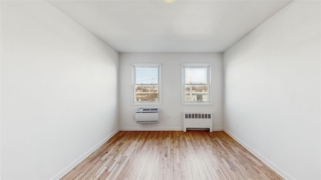 spare room featuring a wall mounted air conditioner, radiator, and light hardwood / wood-style flooring