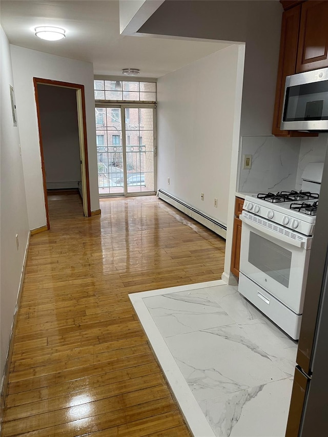 kitchen with white gas range, backsplash, baseboard heating, and light hardwood / wood-style flooring