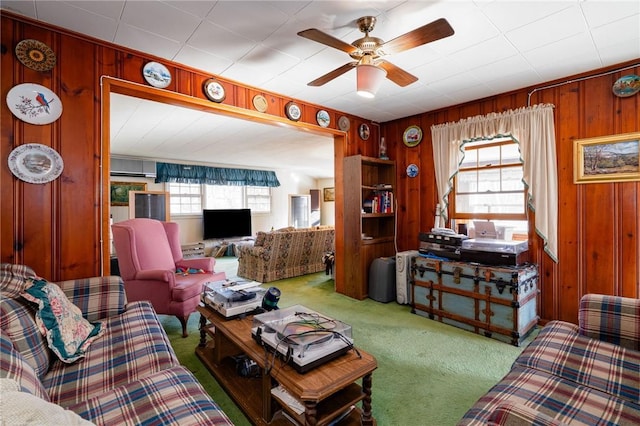 living room featuring ceiling fan, wooden walls, carpet floors, and a wealth of natural light