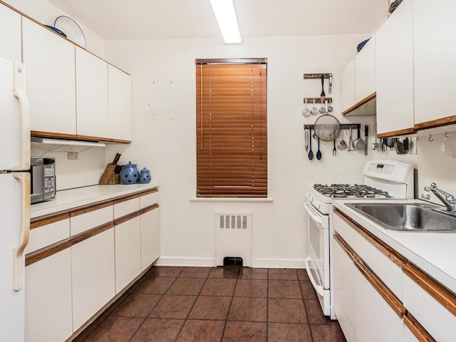 kitchen with sink, white cabinetry, radiator heating unit, dark tile patterned floors, and white appliances