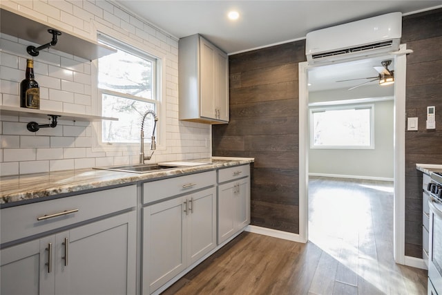 kitchen with an AC wall unit, dark hardwood / wood-style floors, sink, backsplash, and light stone counters