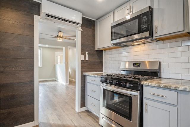 kitchen with appliances with stainless steel finishes, tasteful backsplash, light stone counters, light hardwood / wood-style floors, and a wall unit AC