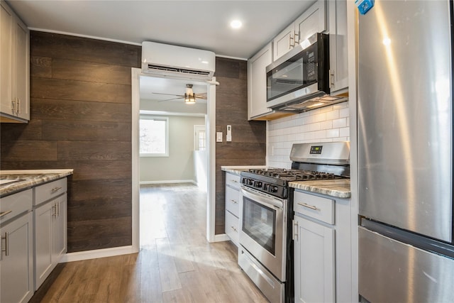 kitchen with light stone counters, backsplash, an AC wall unit, and appliances with stainless steel finishes