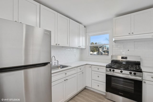 kitchen featuring appliances with stainless steel finishes, sink, white cabinets, decorative backsplash, and light wood-type flooring