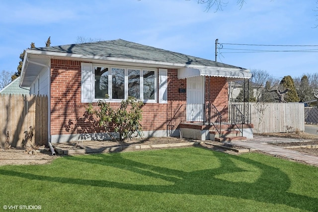 view of front of house with a front yard, brick siding, fence, and roof with shingles