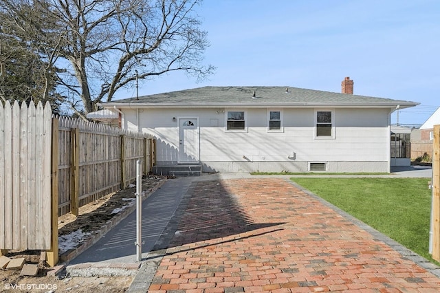 rear view of house featuring entry steps, a chimney, fence, and a lawn