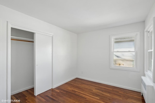 unfurnished bedroom with baseboards, a closet, dark wood finished floors, and radiator