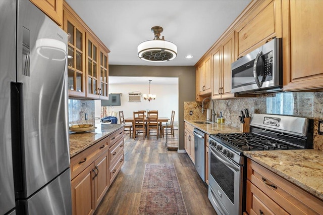 kitchen with appliances with stainless steel finishes, decorative light fixtures, sink, light stone countertops, and dark wood-type flooring