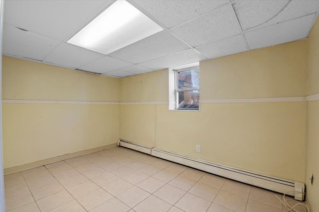 basement with a baseboard radiator, light tile patterned floors, and a drop ceiling